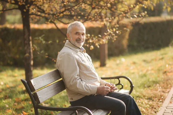 Viejo hombre de pelo gris descansar en el banco en el parque de otoño —  Fotos de Stock