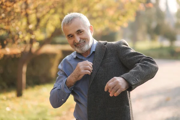 Un bel homme âgé portant une veste grise. Vieil homme barbu aux cheveux gris marche dans le parc d'automne. Fond jaune — Photo