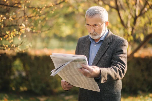 그 노인은 공원에서 신문을 읽었다. 가을에 자라는 노란 나무의 배경 — 스톡 사진