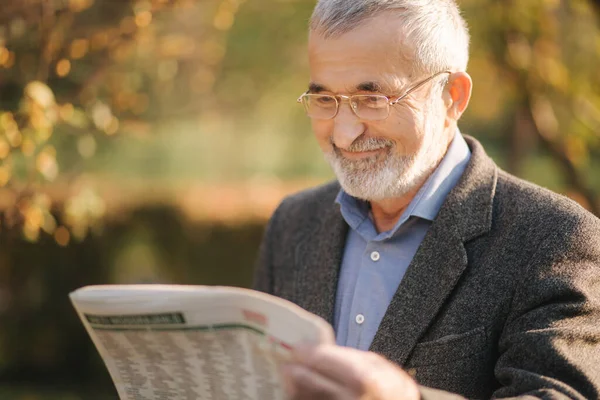 A rangidős ember újságot olvasott a parkban. A sárga fa háttere ősszel — Stock Fotó