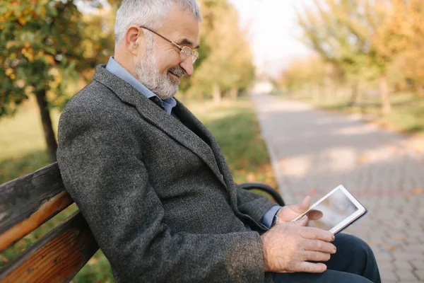 Se burlan de un hombre mayor usando tableta afuera. Vista posterior del anciano sentado en el banco y usando la tableta —  Fotos de Stock