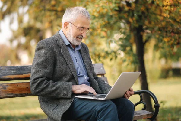 Äldre man använder laptop i parken. Stilig senior man i glasögon arbete utanför — Stockfoto