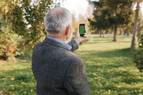 Mock up of elderly man using phone outside. Green screen. Back view of man holding phone at harms length