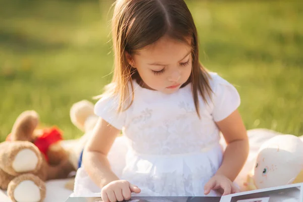 一个可爱的小女孩坐在户外，坐在格子花上看书。快乐微笑的小女孩在日落时花时间在后院 — 图库照片