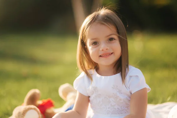 Close-up van Schattig klein meisje zit op de ruit buiten en lees boek. gelukkig glimlach baby meisje tijd doorbrengen op achtertuin in zonsondergang — Stockfoto