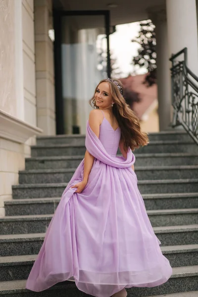 Beautiful young girl in evening lavender dress stand in stairs by restaurant — Stock Photo, Image