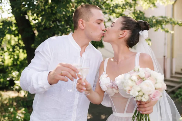 Jeune couple de marié et mariée debout outdors et boire du champagne — Photo