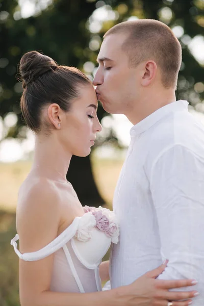 Ritratto ravvicinato di sposo baciare la sposa in fronte davanti a un grande albero. Vista laterale — Foto Stock