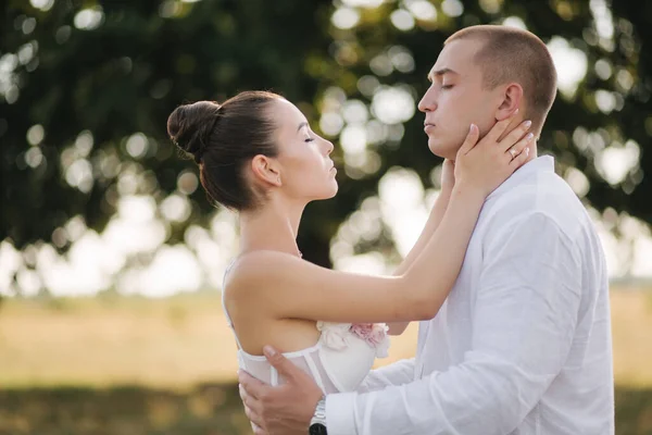 Primer plano retrato de novio beso novia en la frente delante de gran árbol. Vista lateral — Foto de Stock