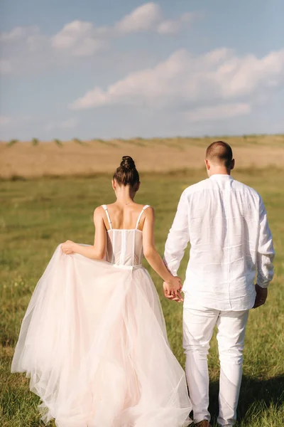 Linda noiva com bonito noivo walkin no campo após a cerimônia de casamento. Recém-casados posando para fotógrafo — Fotografia de Stock