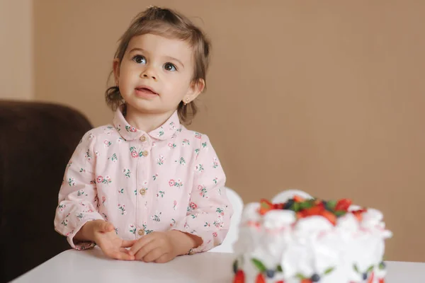 Linda niña de uno y un casco año de edad stand by delicioso pastel de cumpleaños. Dieciocho meses niña muy feliz y se ríe. Comida vegetariana. Sin lactosa y sin gluten . — Foto de Stock