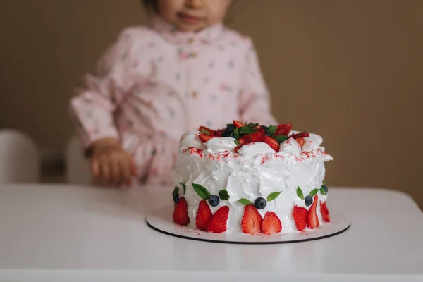 Kislány először kóstolja meg a kétnapos tortát. Aranyos kislány gyönyörű ruha kóstoló torta eperrel — Stock Fotó