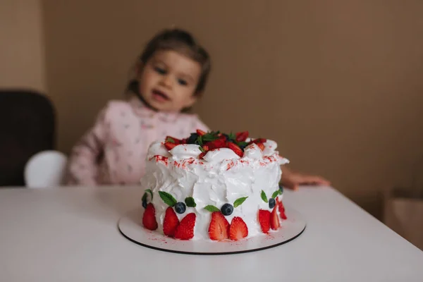 Kislány először kóstolja meg a kétnapos tortát. Aranyos kislány gyönyörű ruha kóstoló torta eperrel — Stock Fotó