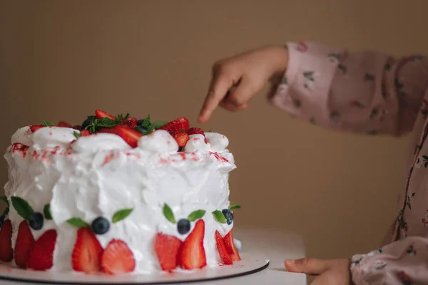Маленькая девочка впервые попробовала торт на день рождения. Милая маленькая девочка в красивом платье дегустации торта с клубникой. Крупный план девушки положить палец в торт — стоковое фото