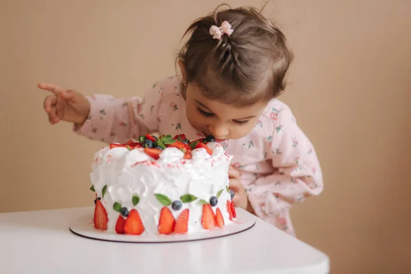 Niña primera vez probar bithday pastel. Linda niña en hermoso vestido degustación de pastel con fresas —  Fotos de Stock