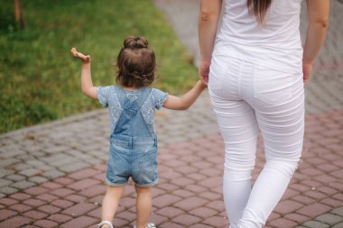 Güzel, genç bir anne, sevimli küçük kızıyla parkta yürüyor. Küçük tatlı bir kız, ev hanımı bir anne eli.