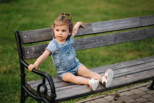 Linda niña en denim sube en el banco en el parque. Feliz niño sonriente en el banco — Foto de Stock