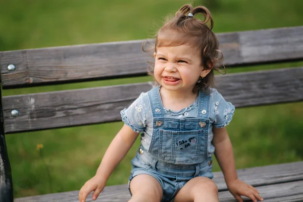 Αξιολάτρευτο κοριτσάκι που γελάει. Όμορφο θηλυκό παιδί σε τζιν κάθεται στον πάγκο στο πάρκο. Χαρούμενο κοριτσάκι χαμόγελο. 18 μήνες — Φωτογραφία Αρχείου