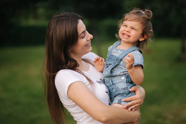 Egy gyönyörű anyuka portréja egy imádnivaló kislánnyal. Boldog család a szabadban. Anya és lánya nevetnek. — Stock Fotó