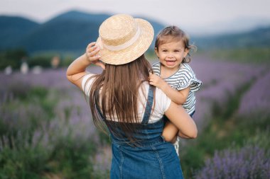 Genç annenin yaz lavanta tarlasında sevimli kızıyla portresi. Aile kot tarzı. Hasır şapkalı kadın.
