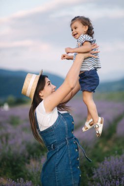 Genç annenin yaz lavanta tarlasında sevimli kızıyla portresi. Aile kot tarzı. Hasır şapkalı kadın. Annenin elindeki küçük kız gülüyor.