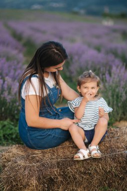 Anne ve küçük kız çiftliğin samanlığında oturuyorlar. Yaz lavanta tarlasının arka planı. Aile kot tarzı
