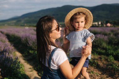 Anne ve küçük kız çiftliğin samanlığında oturuyorlar. Yaz lavanta tarlasının arka planı. Aile kot tarzı. Küçük kız sarıl anneye