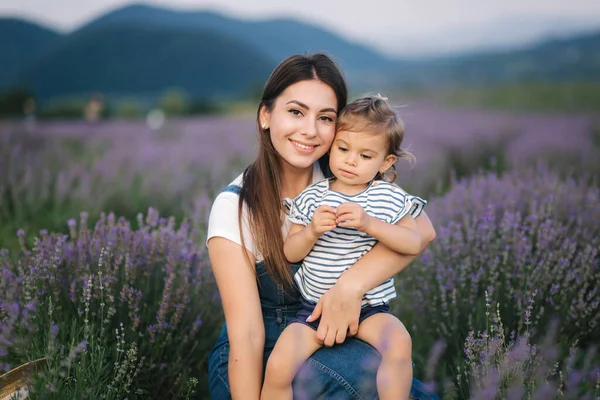 Portretul unei tinere mame atractive, cu o fetiță în câmpul de vară de lavandă. Familie fericită în stil denim — Fotografie, imagine de stoc