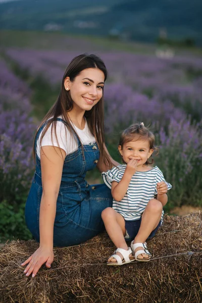 Mamma e figlioletta si siedono sul fieno vicino alla fattoria. Sfondo del campo estivo di lavanda. Stile denim famiglia — Foto Stock