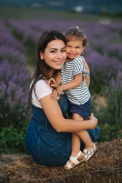 Mama şi fetiţa stau pe fân lângă fermă. Contextul câmpului de lavandă de vară. Stilul denim de familie. Fetiță îmbrățișare mama — Fotografie, imagine de stoc