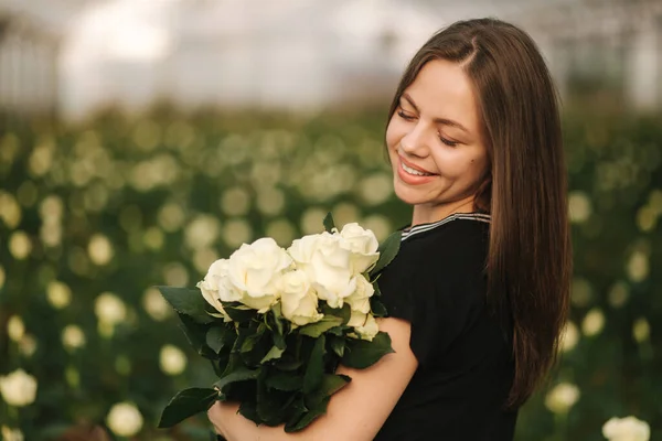 Retrato de hermosa mujer joven en invernadero con ramo de rosas blancas —  Fotos de Stock