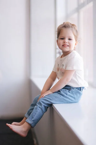Αξιολάτρευτο κοριτσάκι κάθεται στο περβάζι του παραθύρου στο στούντιο — Φωτογραφία Αρχείου