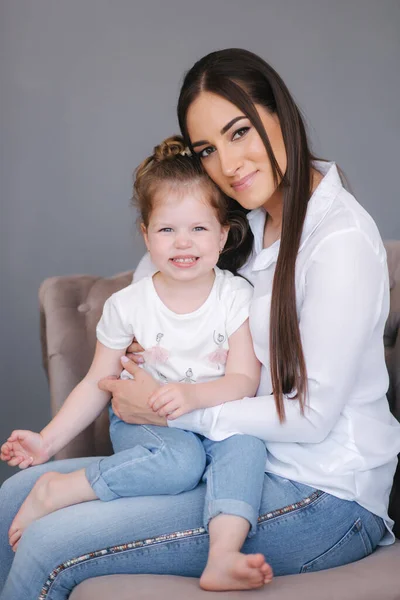 Portret de femeie tânără atractivă cu o fiică drăguță. Mama și fiica stau pe canapea în studio — Fotografie, imagine de stoc