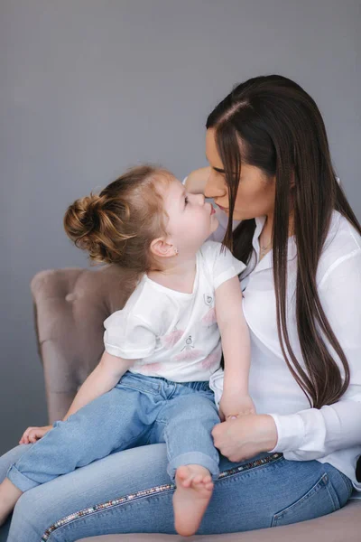 Portret de femeie tânără atractivă cu o fiică drăguță. Mama și fiica stau pe canapea în studio — Fotografie, imagine de stoc