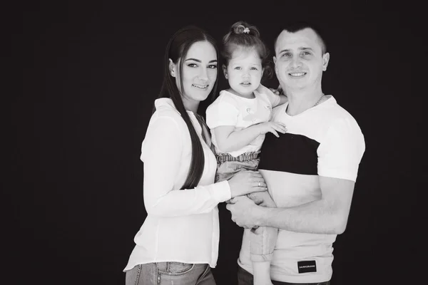 Close up portrait of mom and dad kiss daughter. Studio photosession. Black background. Black and white photo