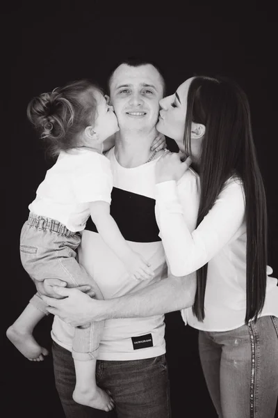 Крупним планом портрет дочки поцілунків мами і тата. Студійна фотосесія. Чорний фон. Чорно-біле фото — стокове фото