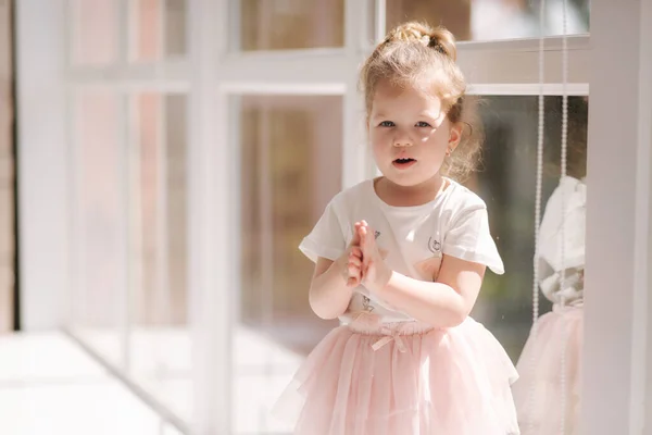 Aranyos kislány hároméves ruhában, aki fényképésznek pózol a stúdióban. A gyönyörű kislány az ablakpárkányon ül. — Stock Fotó