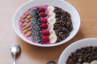 Taze ahududu, yabanmersini, chia tohumu, badem, muz ve çikolata parçacıklı meyve suyu kasesi. Sabah kahvaltısı ahşap masada