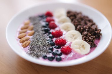 Taze ahududu, yabanmersini, chia tohumu, badem, muz ve çikolata parçacıklı meyve suyu kasesi. Sabah kahvaltısı ahşap masada. Kapat.