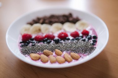 Taze ahududu, yabanmersini, chia tohumu, badem, muz ve çikolata parçacıklı meyve suyu kasesi. Sabah kahvaltısı ahşap masada
