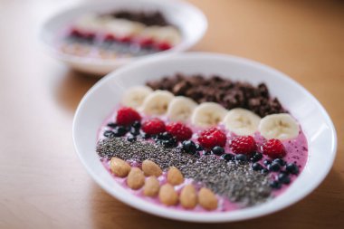 Taze ahududu, yabanmersini, chia tohumu, badem, muz ve çikolata parçacıklı meyve suyu kasesi. Sabah kahvaltısı ahşap masada. İki Ptales Fith Smoothie yayları. Vejetaryen yemeği