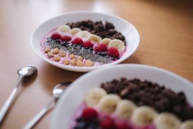 Taze ahududu, yabanmersini, chia tohumu, badem, muz ve çikolata parçacıklı meyve suyu kasesi. Sabah kahvaltısı ahşap masada. İki Ptales Fith Smoothie yayları. Vejetaryen yemeği