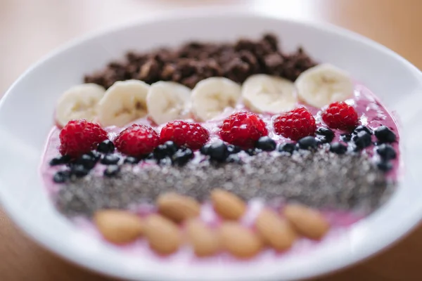 Smoothie bowl with fresh raspberry, blueberry, chia seeds, almonds, banana, and chocolate flakes. Morning breakfast on wooden table. Close up — Stock Photo, Image