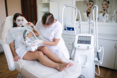 Çekici kadın dinlenirken beyaz eldivenli kozmetik uzmanı midesine radyasyon kaldırma prosedürü uyguluyor. Klinikteki güzel kadın. Tıbbi maskeli güzellik uzmanı.