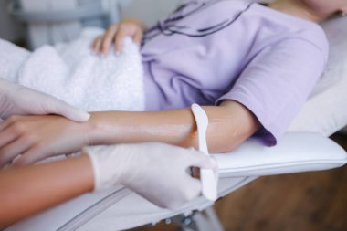 Maskeli genç bayan güzellik uzmanı klinikte lazer tüyü almak için bir kadının eline temas jeli sürüyor. Kapat.