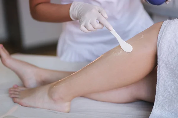 Young woman beautician in mask applies contact gel on the leg of a woman for laser hair removal in medical clinic. Close up — Stock Photo, Image