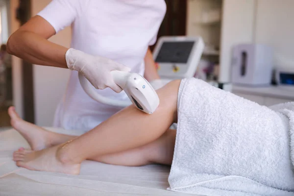 Beautician doing epilation on beautiful girls leg in medical center. Female receiving laser light hair removal treatment for hairless smooth skin at cosmetology salon. Close up — Stock Photo, Image