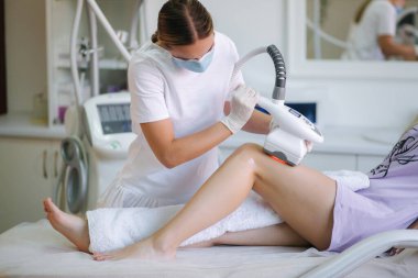 Beyaz eldivenli profesyonel bir dermatolog bir kadının karnına radyoaktivite kaldırma işlemi uyguluyor. Klinikteki güzel kadın. Tıbbi maskeli güzellik uzmanı.