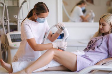 Beyaz eldivenli profesyonel bir dermatolog bir kadının karnına radyoaktivite kaldırma işlemi uyguluyor. Klinikteki güzel kadın. Tıbbi maskeli güzellik uzmanı.