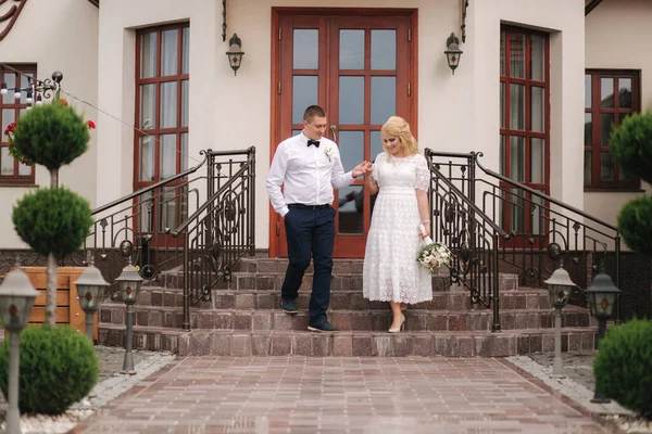 Heureux jeunes mariés marchant à l'extérieur. Femme aux cheveux blonds et jeune homme en chemise blanche — Photo